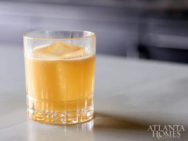 Orange cocktail in a glass with ice and a citrus peel garnish.