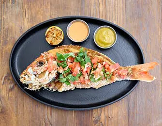 Whole fried fish topped with chopped tomatoes and herbs, served with lemon and two dipping sauces