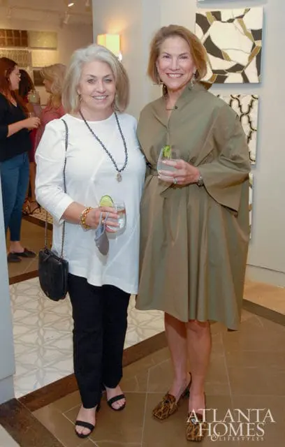 Two women smiling, one in a white top and black pants, the other in a khaki dress.