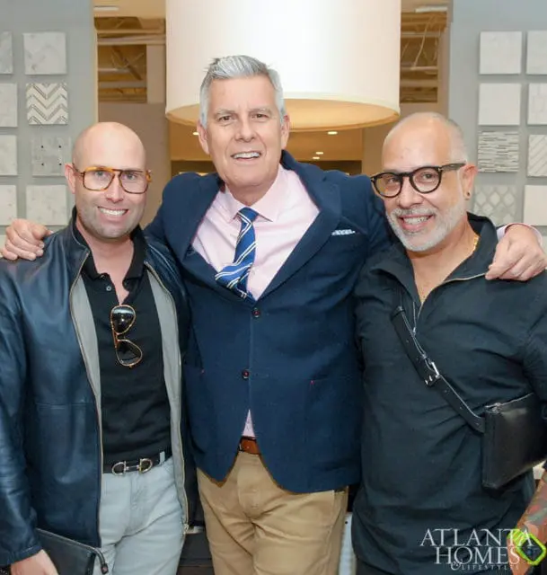 Three men posing for a photo, two on the sides with arms around the man in the middle.
