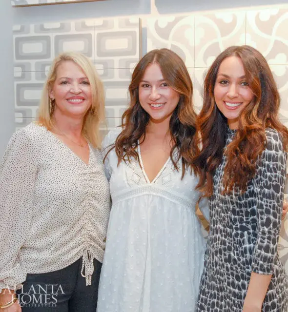 Three women smiling in front of a tiled wall. Atlanta Homes & Lifestyles logo in bottom left.