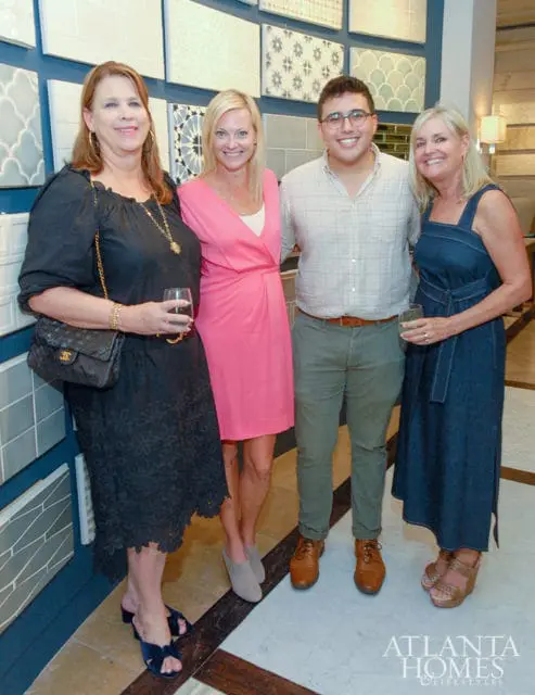 Four people pose in front of a wall of decorative tiles.