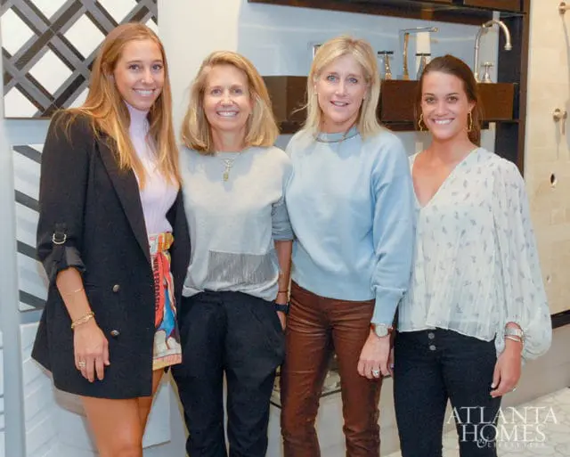 Four women posing in front of a display of faucets and tiles. Atlanta Homes & Lifestyles logo in