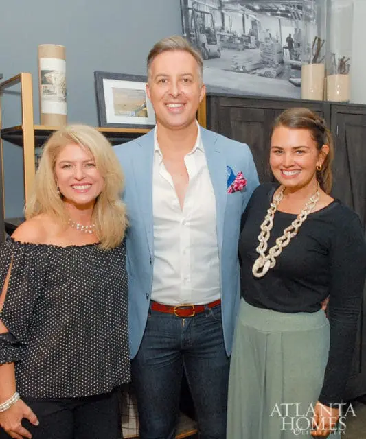 Three people smiling, two women and one man. The man wears a light blue blazer.