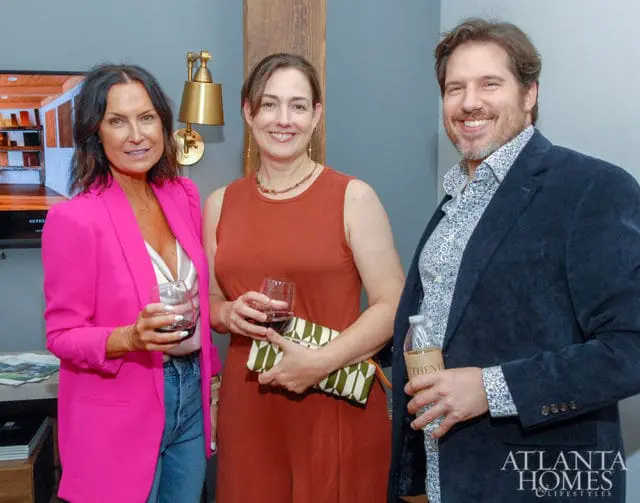 Three people smiling, two women and one man, holding drinks.