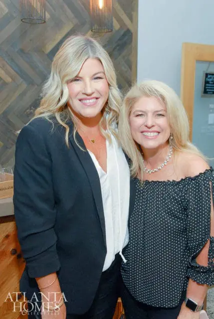 Two women smiling, one in a black blazer and white shirt, the other in a black polka dot
