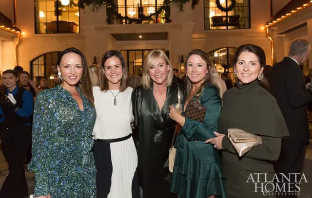 Five women in formal attire pose for a photo at an event with a building in the background.