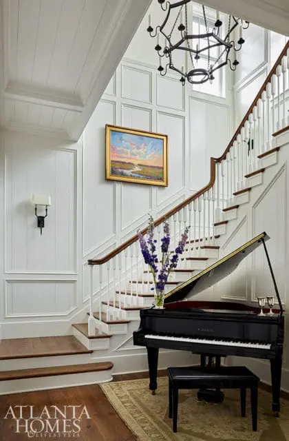 Grand piano in entryway with white paneled walls and staircase