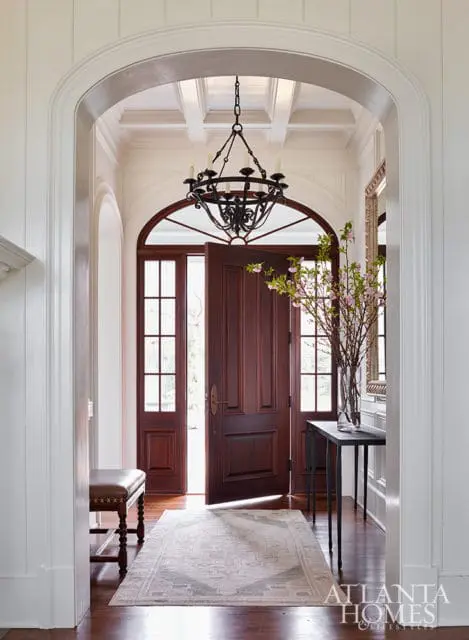 Entryway with arched doorway, double wooden doors, chandelier, bench, and console table