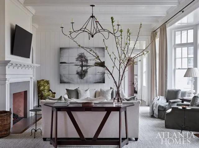 Living room with white shiplap walls, a gray stone fireplace, a large black chandelier, and a sofa with decorative pillows. A dark wood console table sits in front of the sofa.