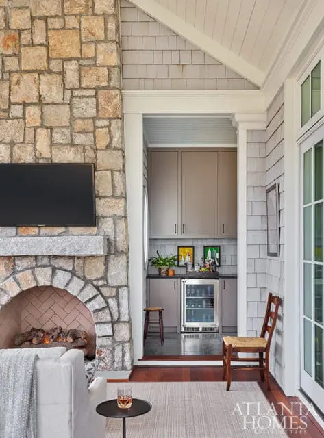 Living room with stone fireplace, bar area with grey cabinets and mini-fridge, and wood floors.