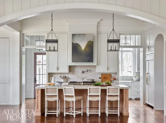 White kitchen with marble backsplash, island with wood base, and four upholstered bar stools.
