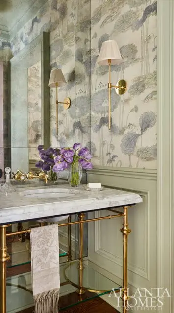 Powder room with floral wallpaper, marble vanity, and brass sconces.