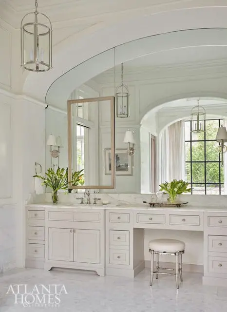 White bathroom with marble countertops, light gray cabinetry, and a vanity stool.