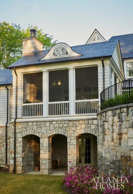Stone arched entryway below a screened porch with white columns and railings.