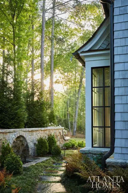 Stone retaining wall with arched fountain feature and stepping stone path. Tall trees in background.