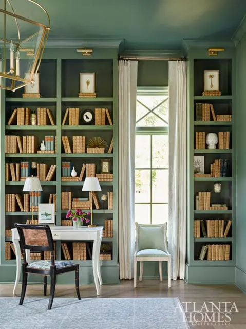 Green study with built-in bookshelves filled with books, a white desk, and two chairs.