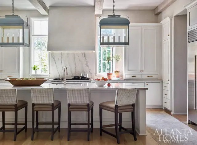 White kitchen with marble backsplash, island with bar stools, and pendant lights.