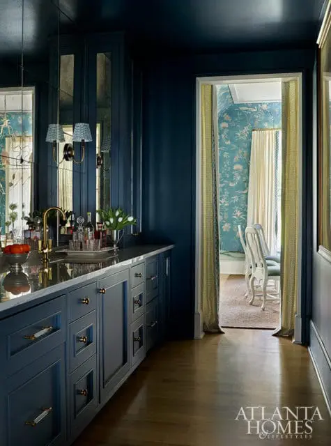 Dark blue bar area with marble countertop and brass fixtures, opening to a dining room with floral