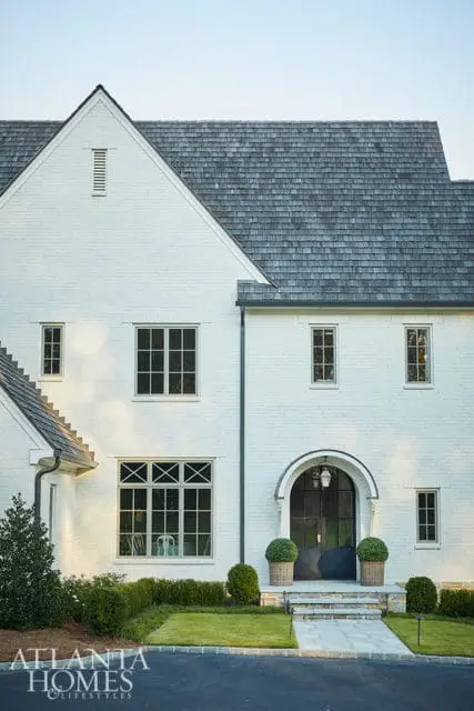 White brick house with arched entryway, dark metal doors, and shingle roof.