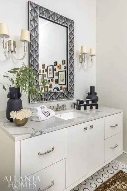 White vanity with marble countertop, geometric mirror, and sconce lighting.