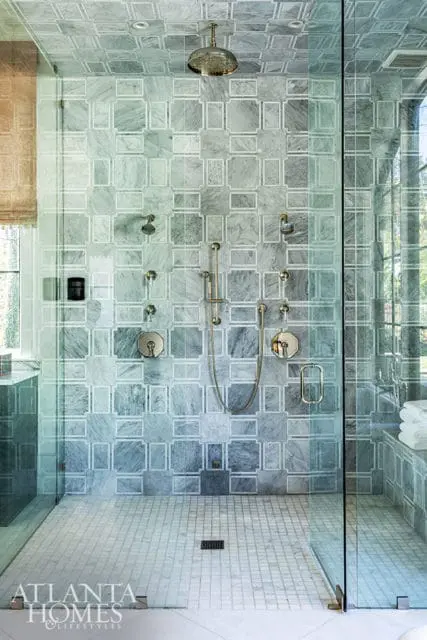 Shower with marble tile walls and floor, brass fixtures, and glass enclosure