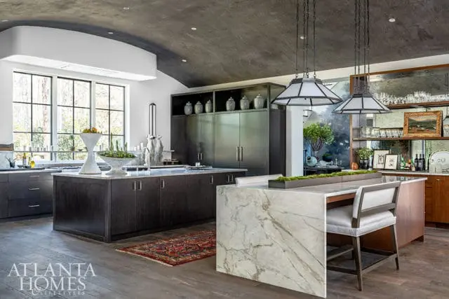 Dark wood kitchen island with marble waterfall edge and seating. Large window behind.