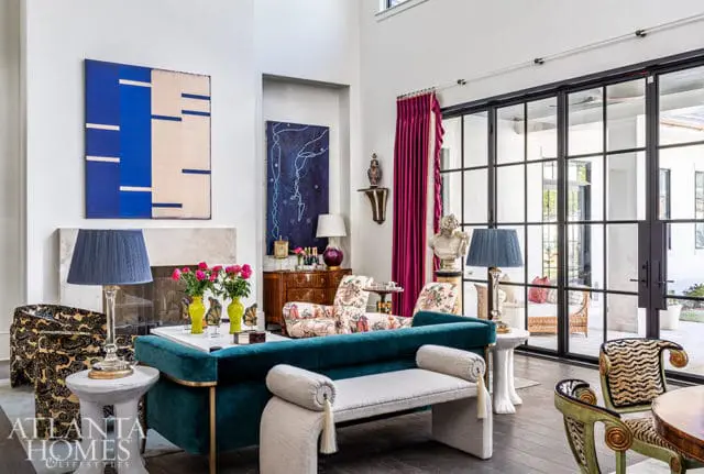 Living room with teal sofa, patterned chairs, abstract art, and large glass doors.
