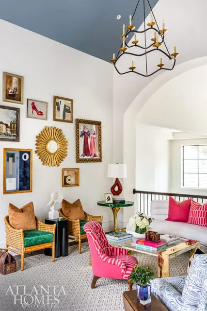 Living room with blue ceiling, gallery wall, rattan chairs, and pink striped armchair.