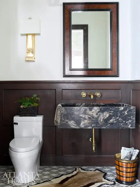 Powder room with dark wood paneling, marble sink, brass fixtures, and geometric floor tile