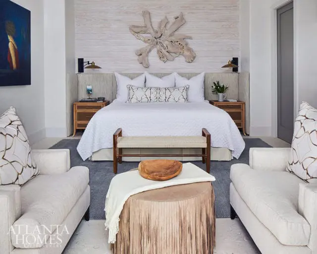 Bedroom with white bedding, wood accents, and upholstered chairs. Atlanta Homes & Lifestyles logo