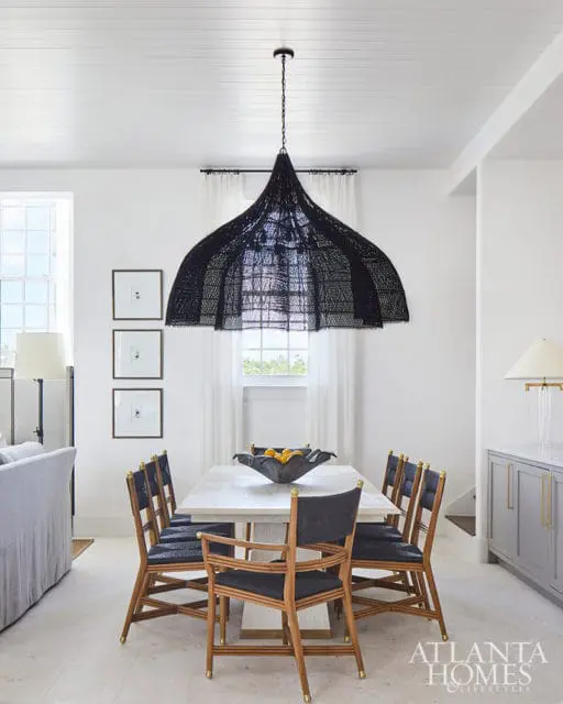 Dining room with white table, black woven chandelier, and gray cabinets.