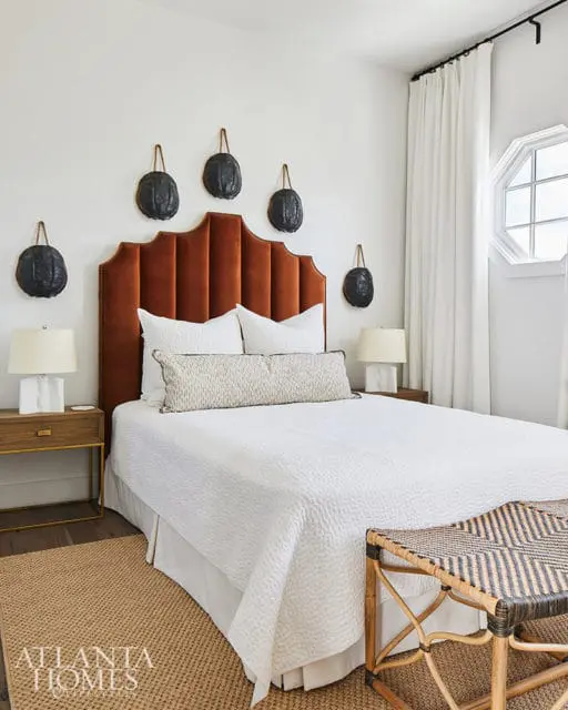 Bedroom with orange velvet headboard, white bedding, and dark wall decor