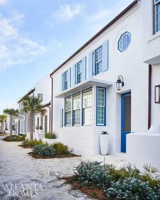 White stucco buildings with blue shutters and doors, palm trees, and stone pathway.