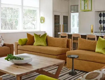Living room with mustard sofas, green and orange pillows, wood coffee table, and bar area with