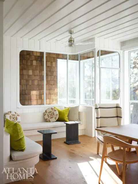 Sunlit room with built-in bench seating, wood-shingled accent wall, and wooden dining set.