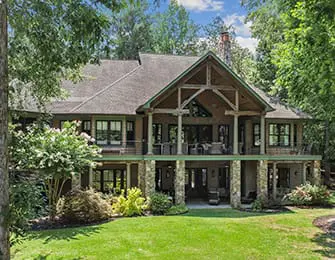 Large house with stone pillars and multiple balconies surrounded by trees and green lawn.