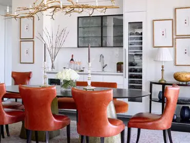 Dining room with orange leather chairs, dark oval table, wine fridge, and gold branch chandelier.