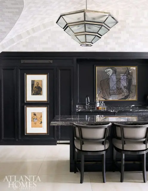 Black kitchen island with marble countertop, two bar stools, and artwork on black cabinetry.