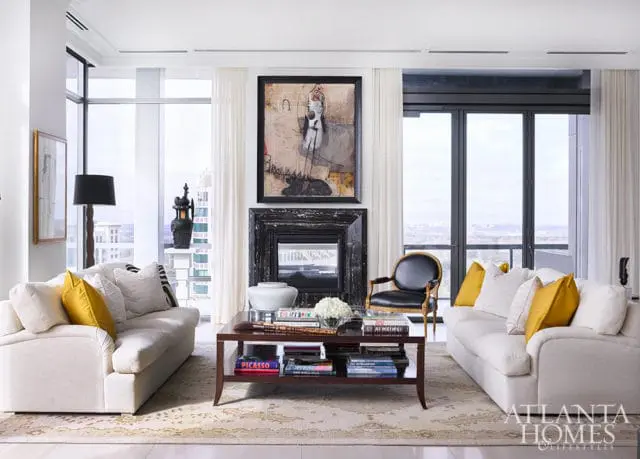 Living room with two cream sofas, yellow pillows, dark wood coffee table with books, and fireplace