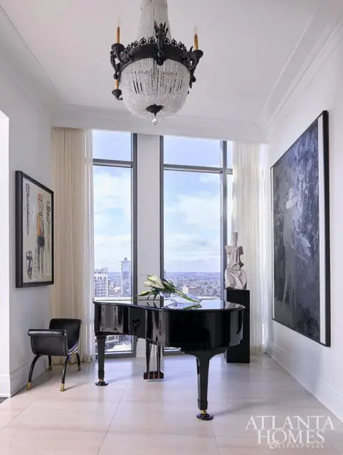 Black grand piano and black chair in a room with large windows and a crystal chandelier.
