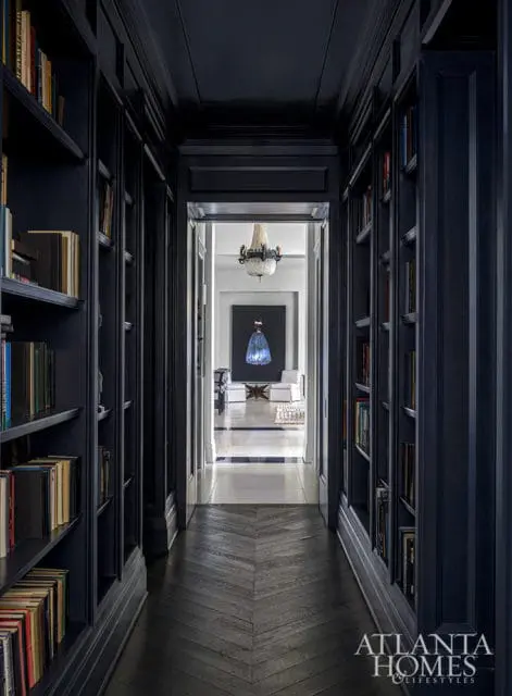 Dark blue hallway with built-in bookshelves and chevron wood floor, opening to a living room with