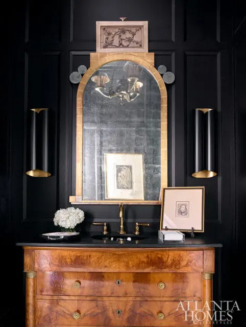 Black paneled walls with antique gold mirror, brass faucet, and wood vanity