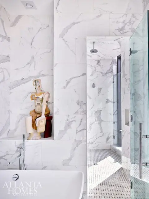Marble tiled bathroom with a sculptural art piece and a glass-enclosed shower.
