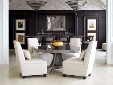 Dining area with four cream upholstered chairs around a round metal table with glass top.