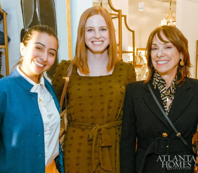 Three smiling women posing for a photo. The woman on the left wears a blue jacket and white shirt