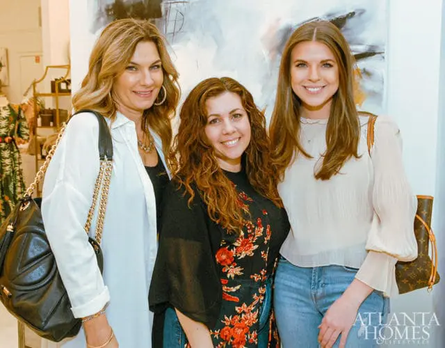 Three women smiling, with abstract art behind them. Atlanta Homes & Lifestyles logo in corner.