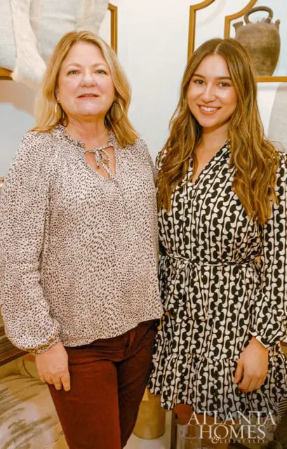 Two women smiling, one in a leopard print blouse and maroon pants, the other in a black and white