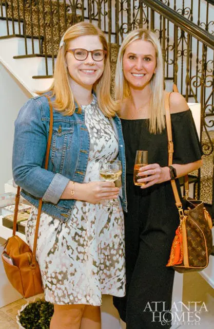 Two women smiling, one in a denim jacket and patterned dress, the other in a black off-the-shoulder