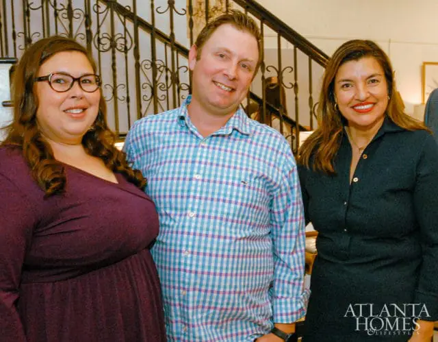 Three people posing in front of a decorative staircase. Atlanta Homes & Lifestyles logo in corner.